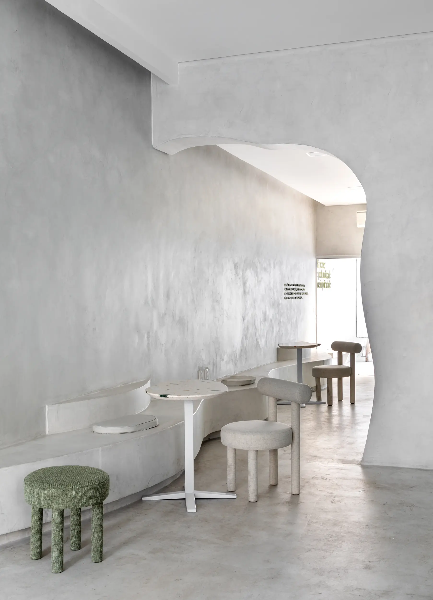 Ambiente interno do projeto Green Blood com parede texturizada e mesas minimalistas, por Studio Guilherme Garcia